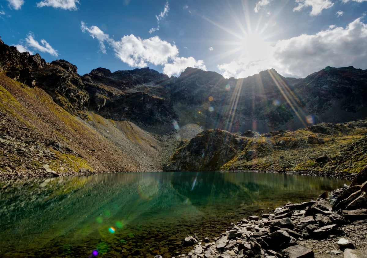 Fine Art Print des Schönrinnenkarsee in den Alpen Österreichs in Gries mit Sonnenstern und dramatischen Wolken, im See spiegelt sich das Ufer